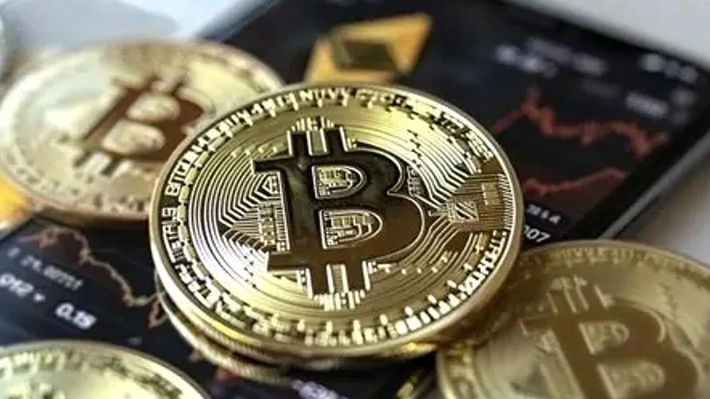 Monedas de bitcoin junto a un celular con gráficos, tras el hackeo a Binance por US$6.300 millones